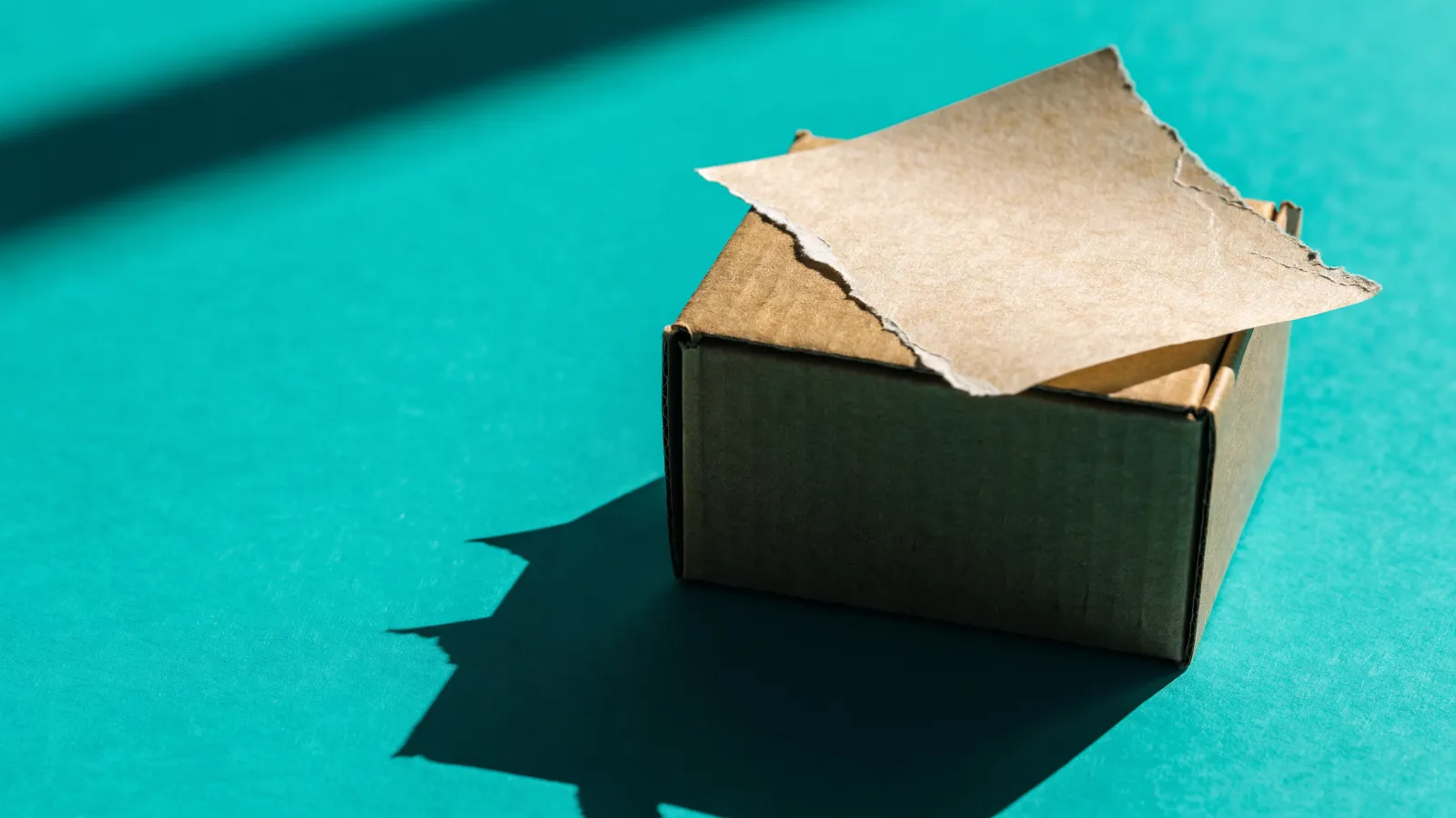 Una etiqueta de precio con una esquina arrancada sobre una caja de envío de cartón, sobre fondo turquesa