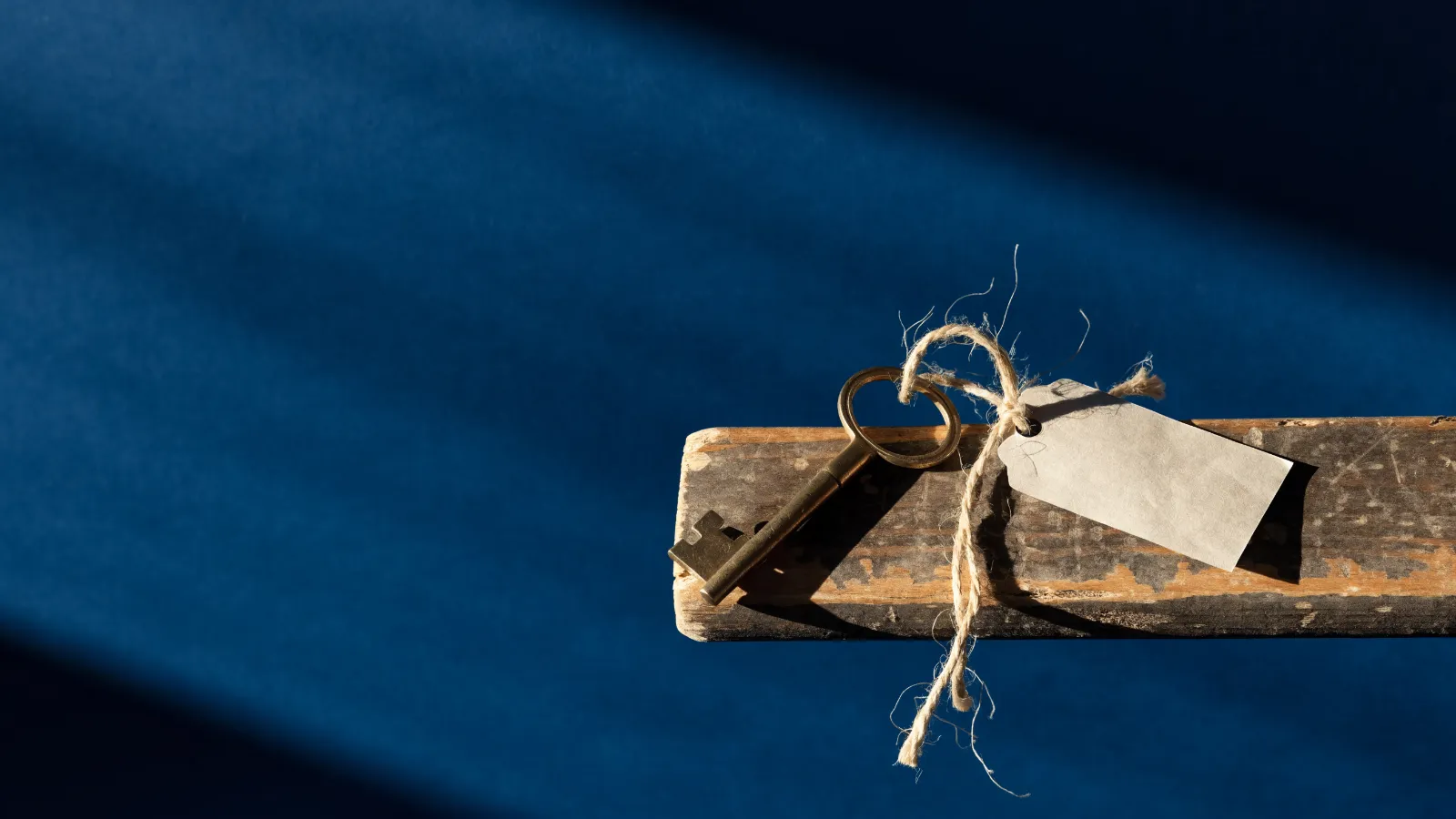Una llave antigua atada con cordel a una etiqueta de papel en blanco sobre un umbral de madera, sobre fondo azul noche