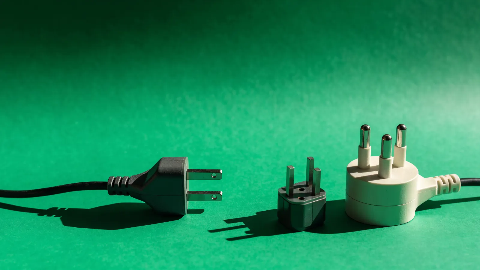 Dos clavijas eléctricas distintas con un adaptador entre ellas, sobre fondo verde