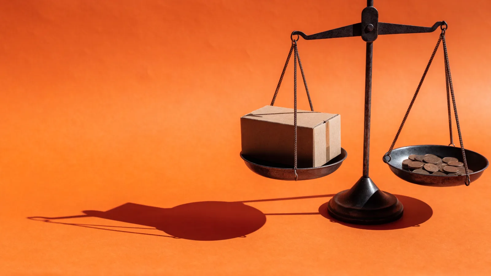 Una balanza con una caja de envío que pesa más que unas monedas en el otro plato, sobre fondo naranja