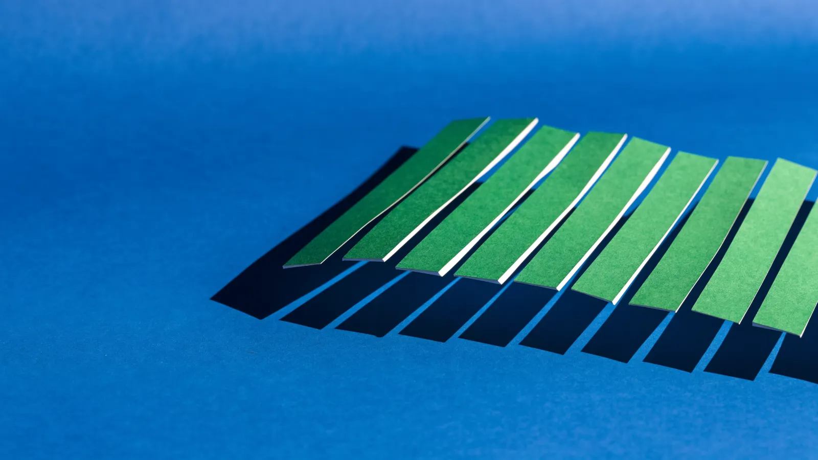 Una hoja de papel verde cortada en tiras con las dos últimas faltantes, sobre fondo azul