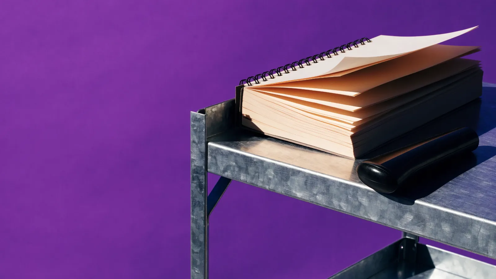 Una libreta de pedidos gastada junto a un lector de código de barras en un anaquel, sobre fondo violeta