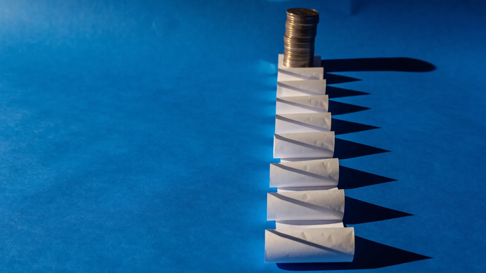 Un ticket largo doblado en doce secciones iguales con una pila de monedas al inicio, sobre fondo azul