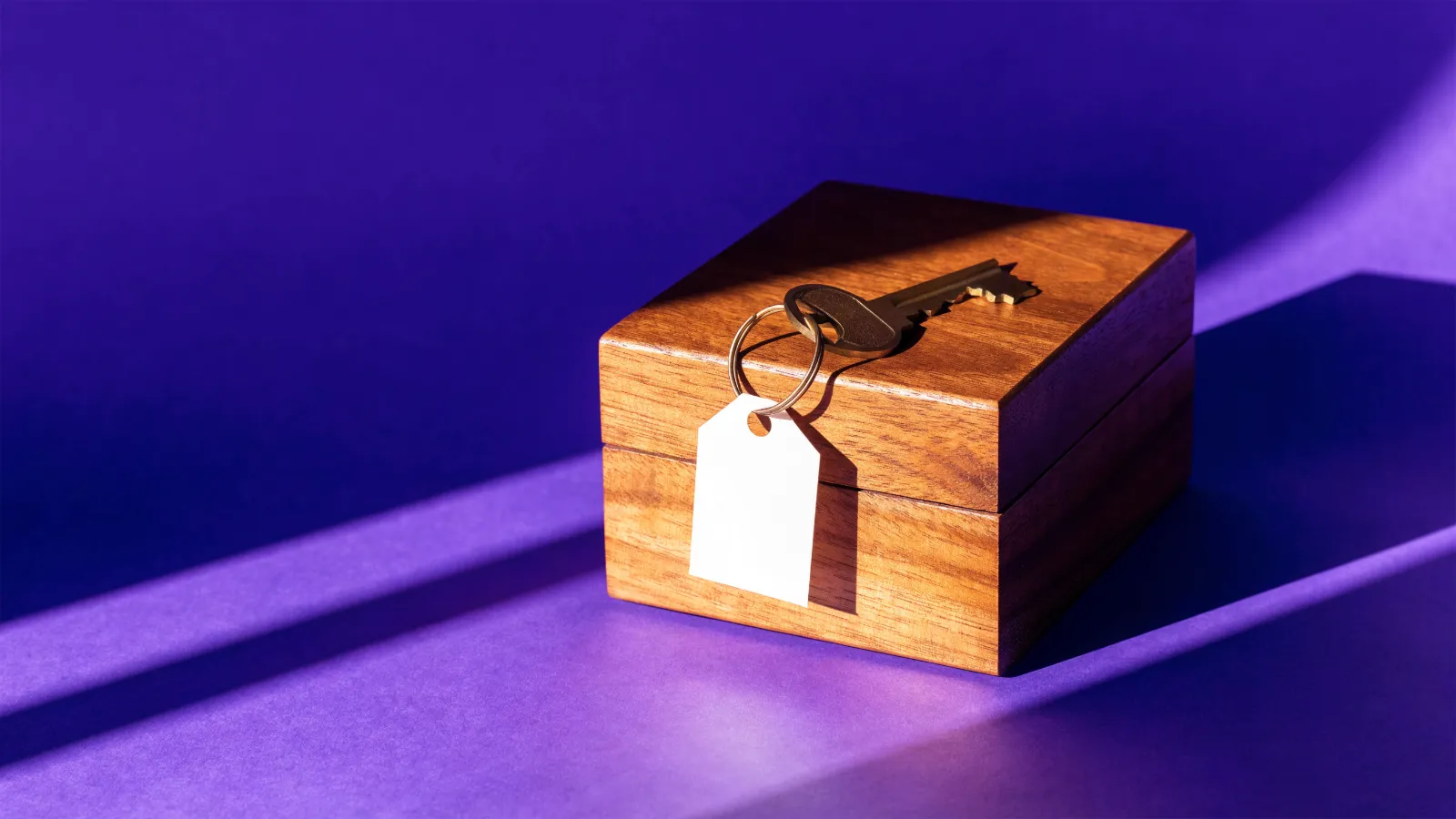 Una llave con etiqueta de papel sobre una caja de madera para catálogo, sobre fondo violeta