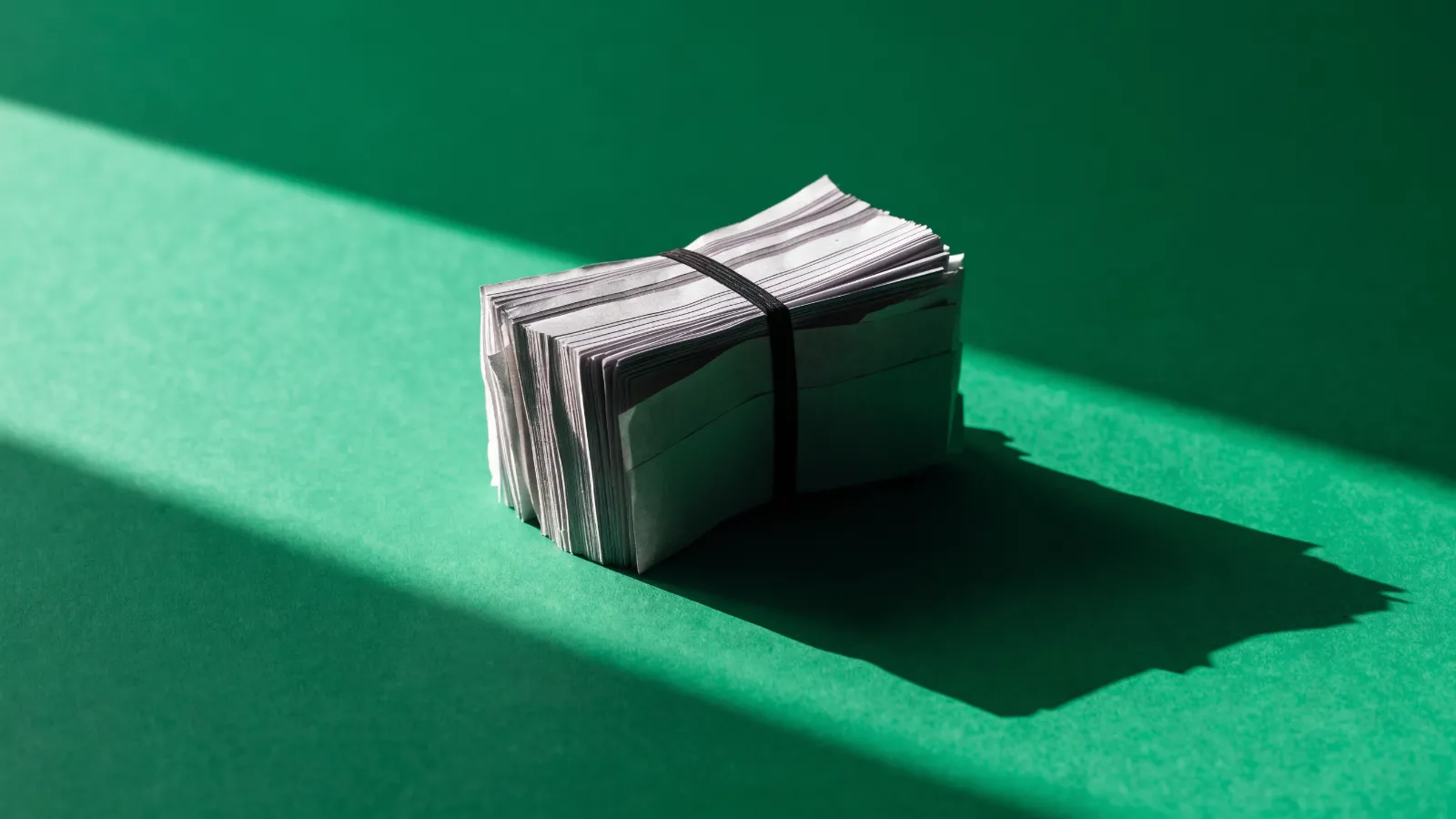 Decenas de tickets de papel atados en un solo fajo con una liga, sobre fondo verde