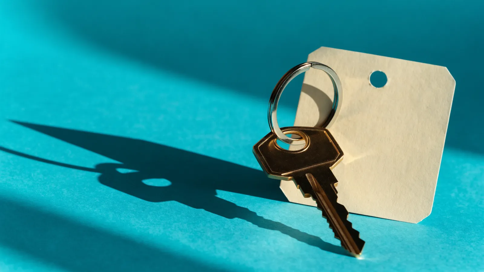 Una llave de casa en su argolla junto a un boleto de guardarropa en blanco, sobre fondo turquesa